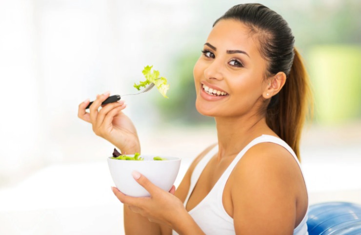 donna che sorride mentre mangia un'insalata