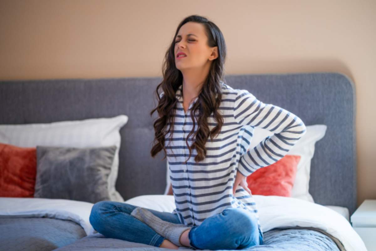 donna seduta sul letto con mal di schiena