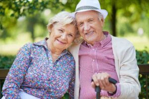 uomo e donna anziani che sorridono seduti su una panchina al parco