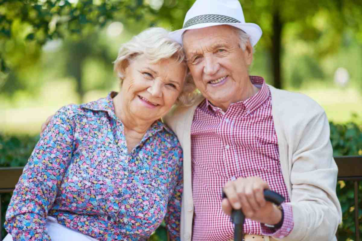 uomo e donna anziani che sorridono seduti su una panchina al parco